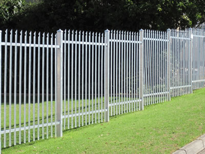White steel palisade fence in ladder type, installed on the grass land, the posts are deeply buried in the ground.